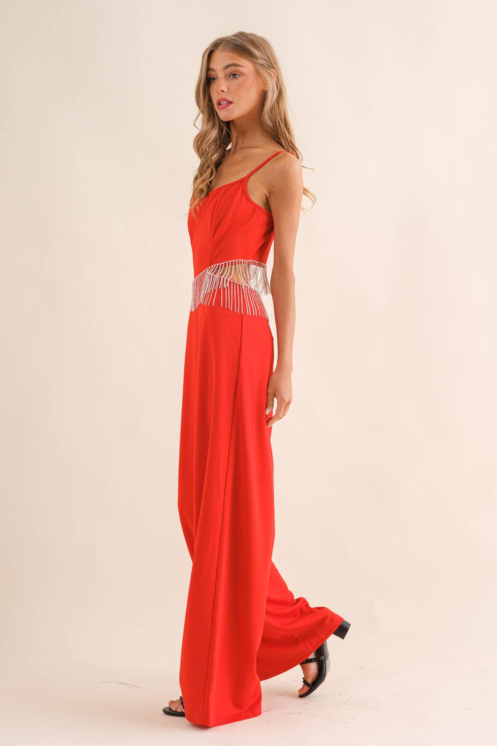 Red jumpsuit with spaghetti straps and crystal fringe waist detail.