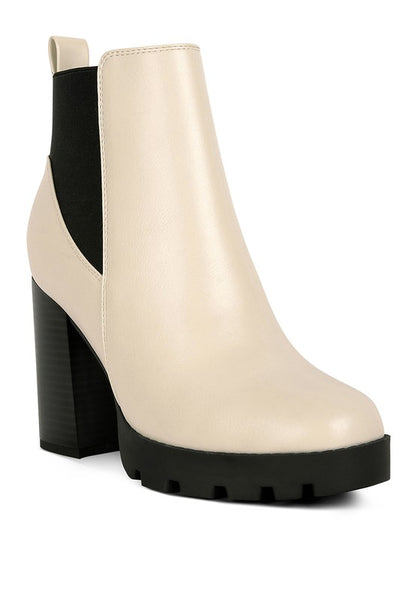 Beige ankle boot with black heel, made of faux leather and features a chunky lug sole.