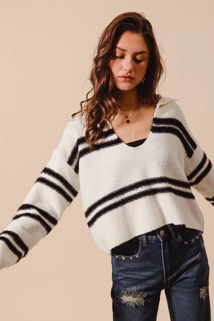 White and black striped sweater with V-neck, long sleeves, and soft knit fabric.