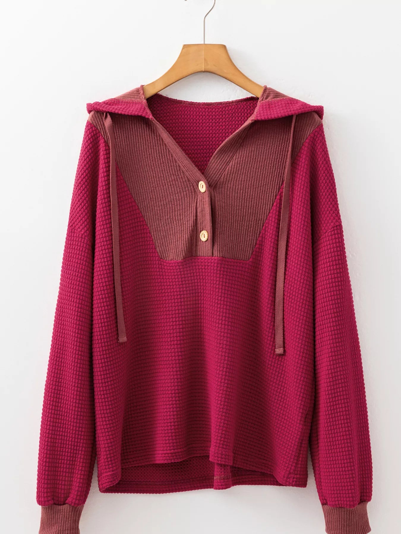 Magenta and mauve waffle-knit hoodie with buttons and drawstrings, made of textured cotton fabric.