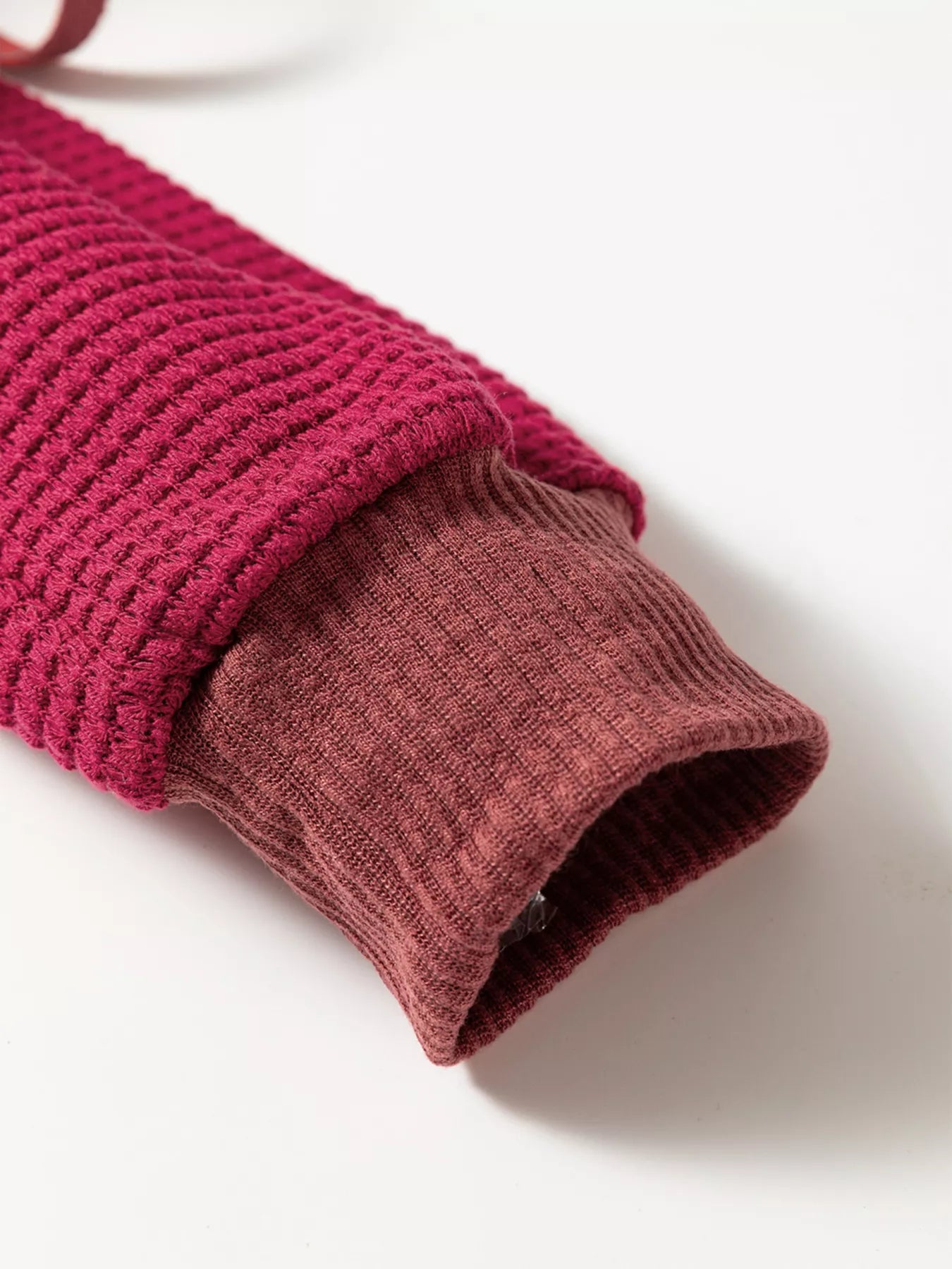 Dark pink waffle knit hoodie sleeve with ribbed cuff and soft textured fabric.