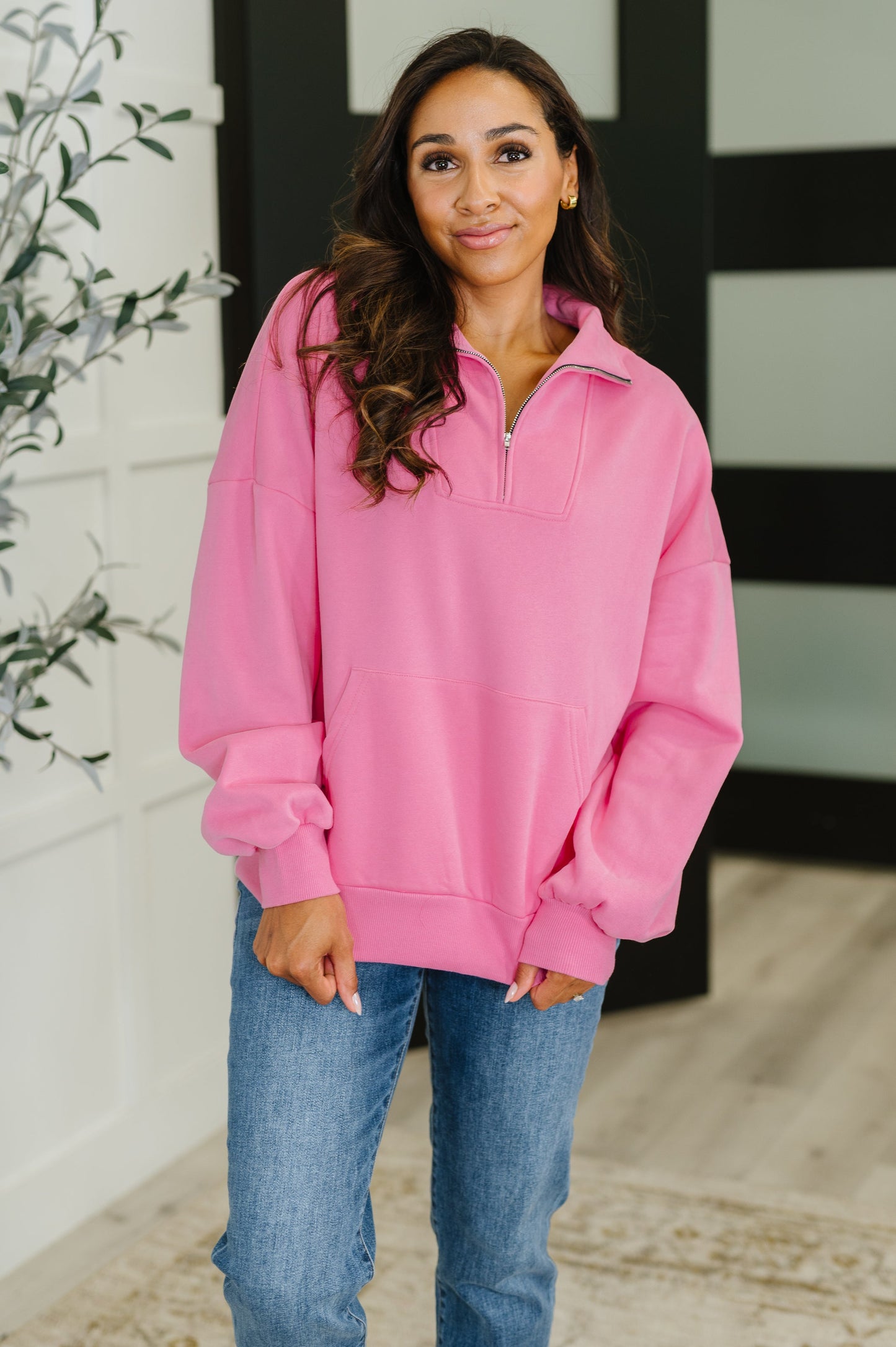 Woman wearing a pink pullover with a zipper, standing indoors.