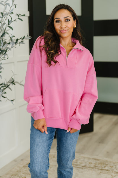 Woman wearing a pink pullover with a zipper, standing indoors.