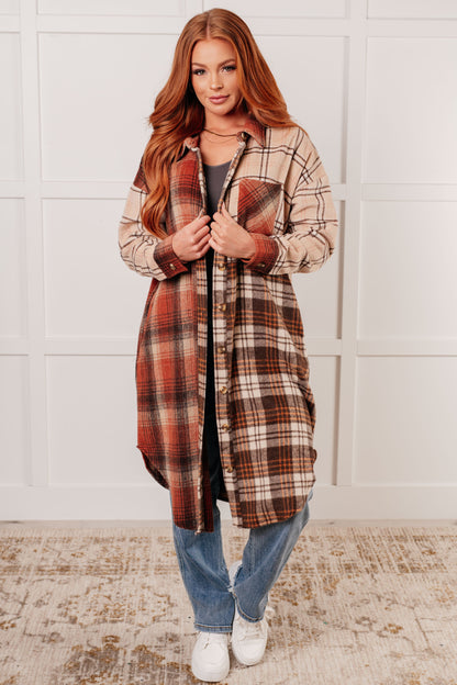 Woman wearing a plaid coat in a room with a white wall and patterned rug.
