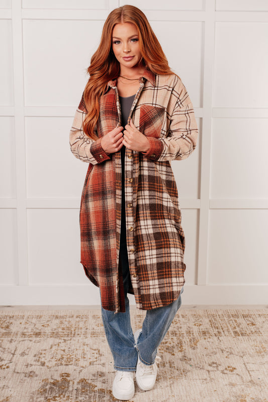 Woman wearing a plaid coat in a room with a white wall and patterned rug.