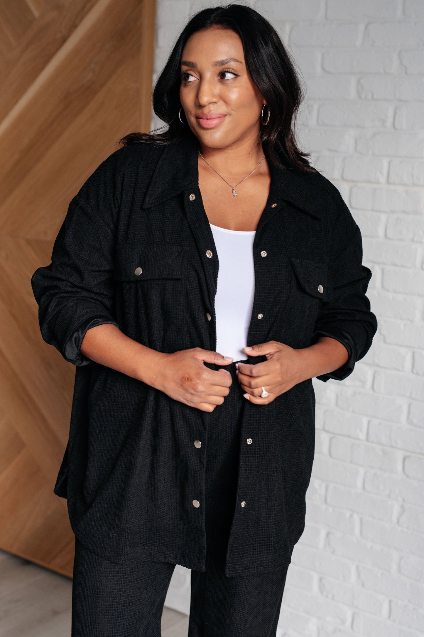 Woman wearing a black jacket against a white brick wall.