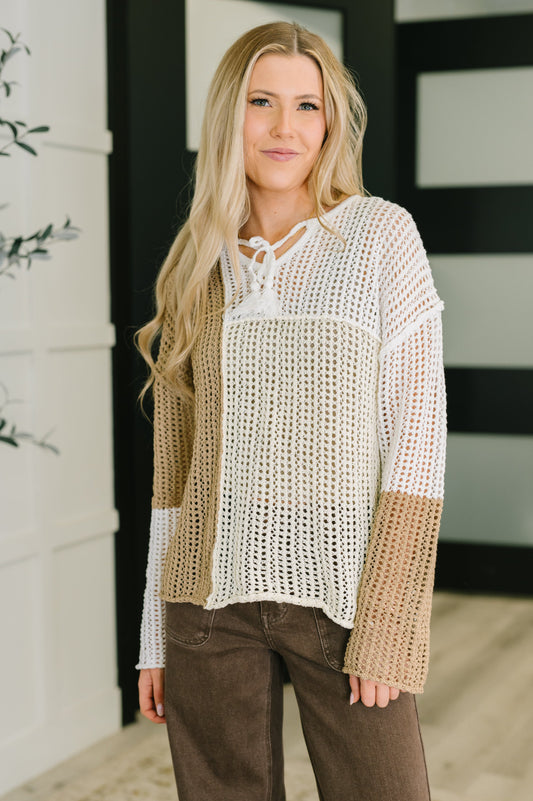 Woman wearing a beige and white knitted sweater with brown pants indoors.