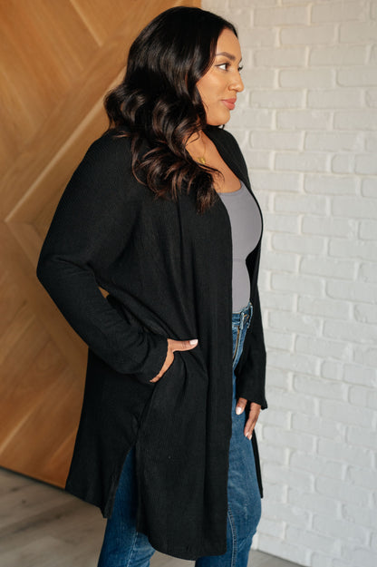 Black ribbed knit cardigan with open front and side slits for added comfort and layering.