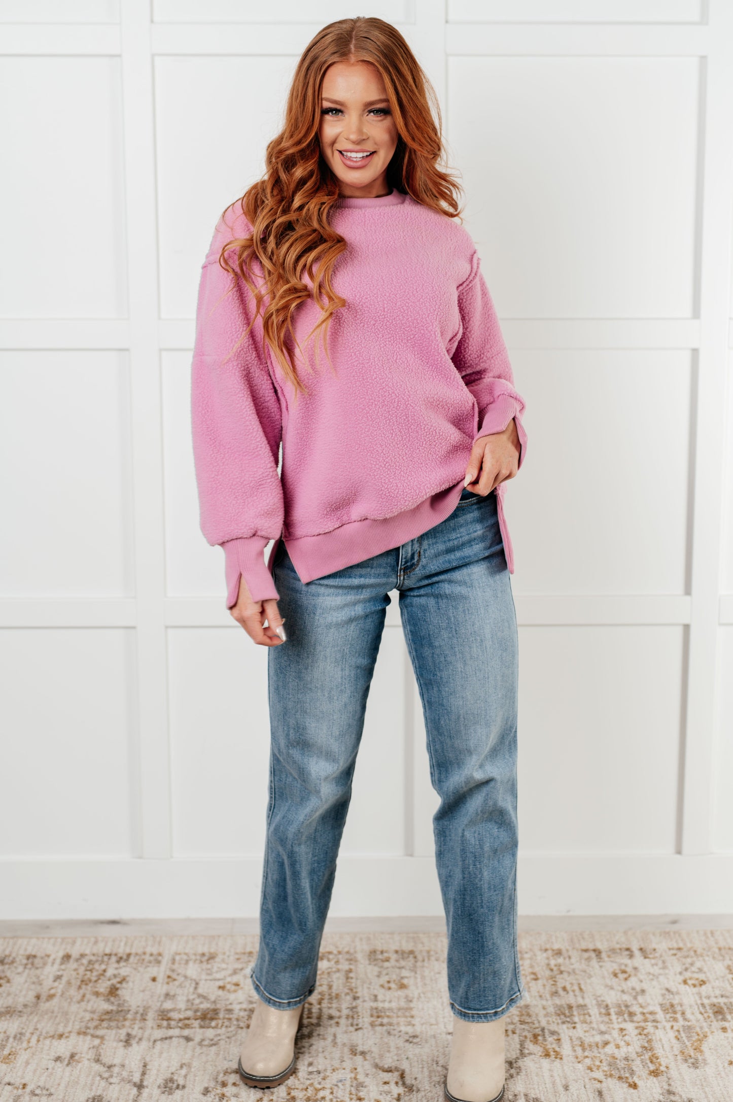 Woman wearing a pink sweater and blue jeans against a white wall.