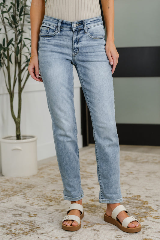 Person wearing light blue jeans standing indoors with a plant and wall in the background