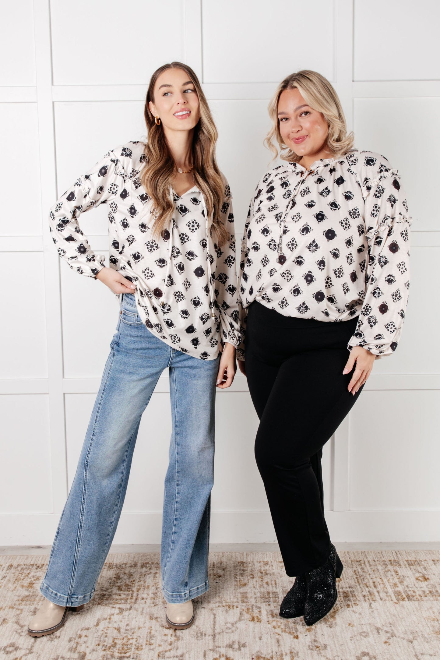 Two women wearing matching patterned tops against a white paneled wall.