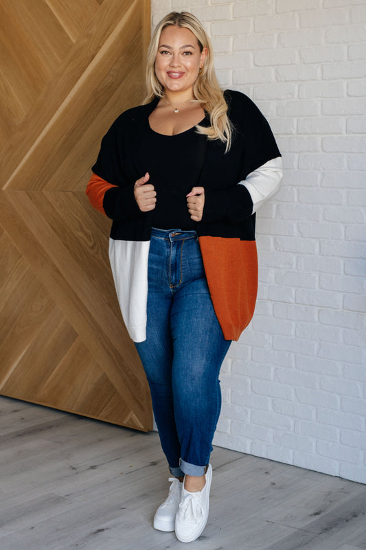 Woman wearing a colorful sweater and blue jeans standing against a wooden and brick wall.